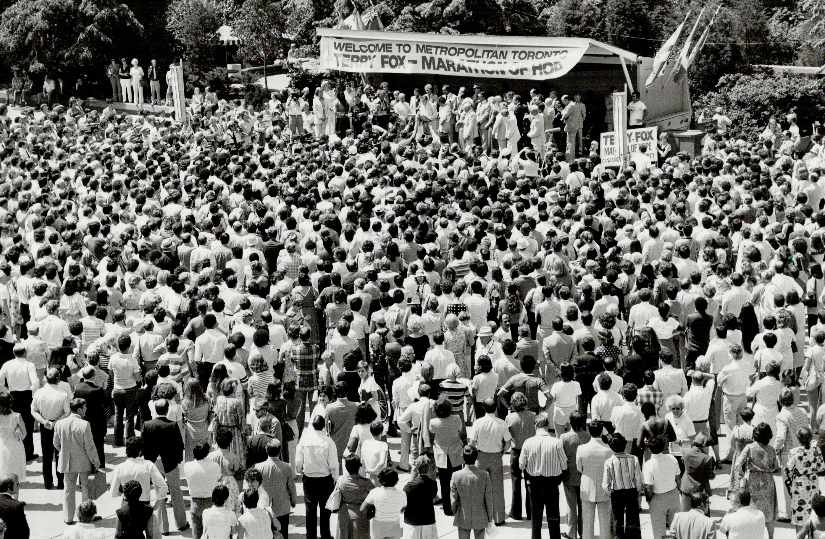A large crowd gathers at a 1980 event in Metropolitan Toronto for Terry Fox's Marathon of Hope, with a banner welcoming him and a stage visible in the background