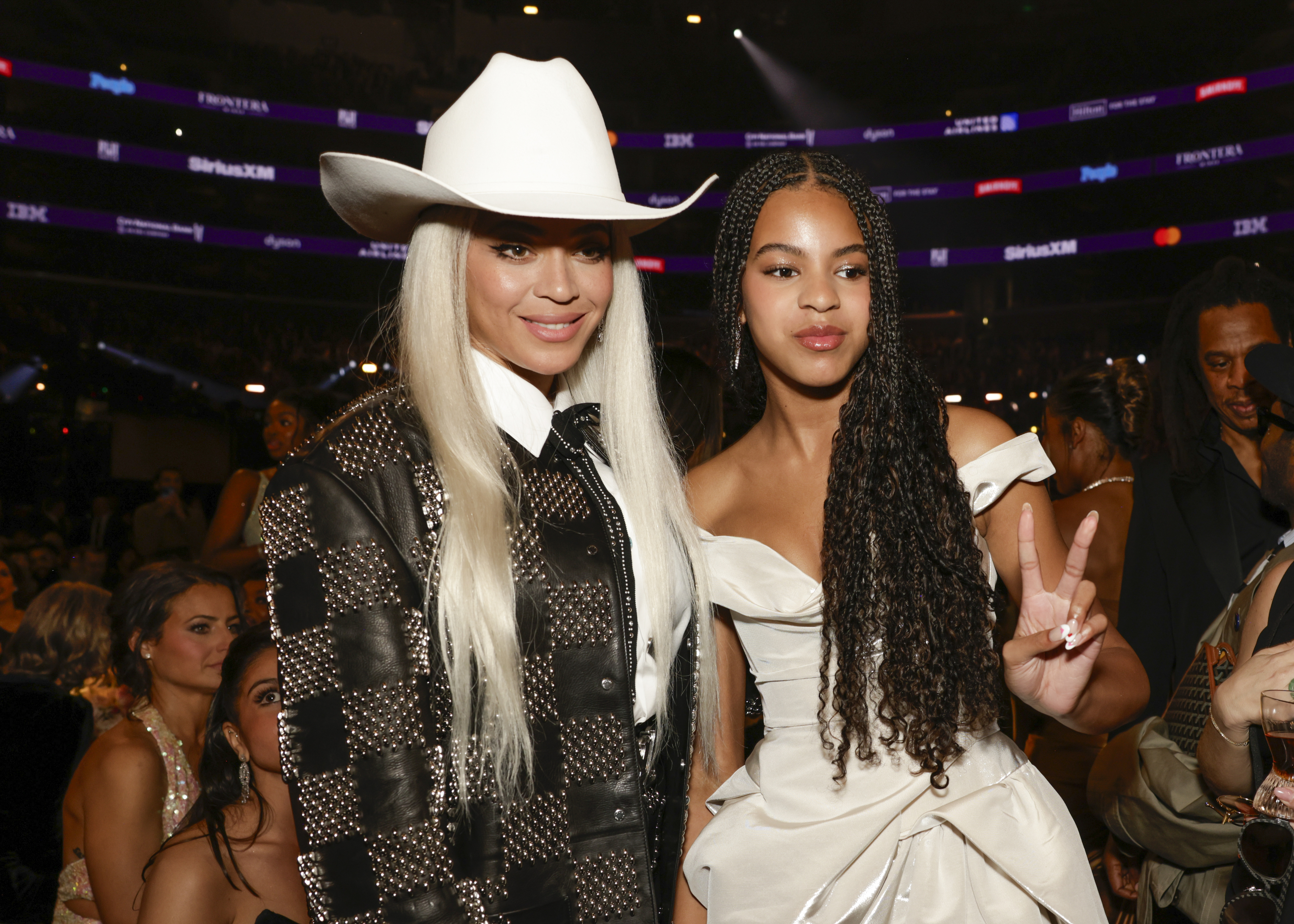 Beyoncé in a checkered outfit and cowboy hat, standing next to Blue Ivy Carter in an off-the-shoulder gown, both posing at an awards show