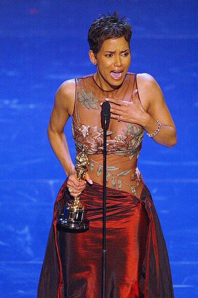Halle Berry holds an Oscar while giving a speech, wearing an elegant sheer dress with floral designs and a satin skirt
