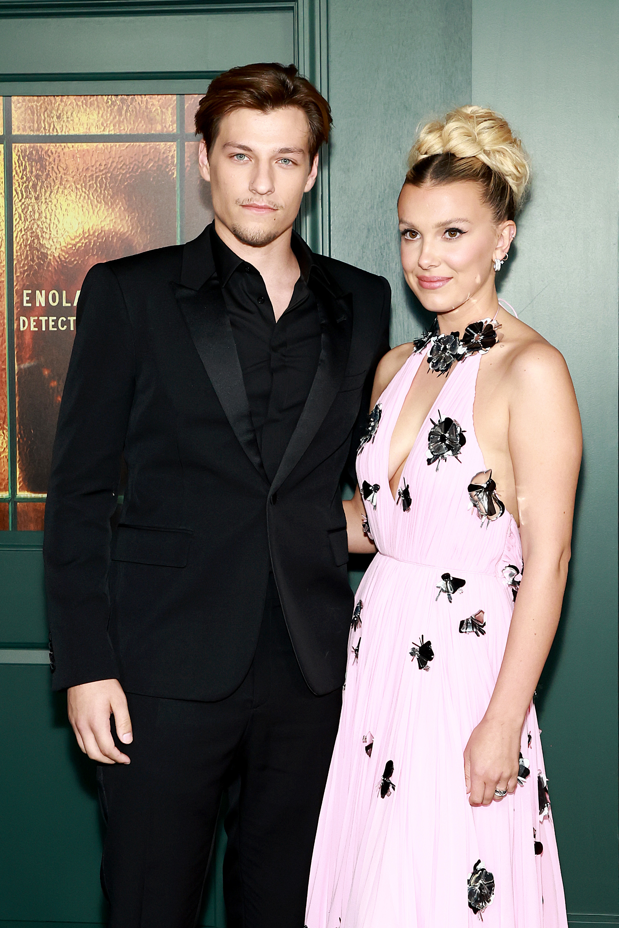 Jake Bongiovi, in a suit and Millie Bobby Brown, in a floral dress, pose together at an event