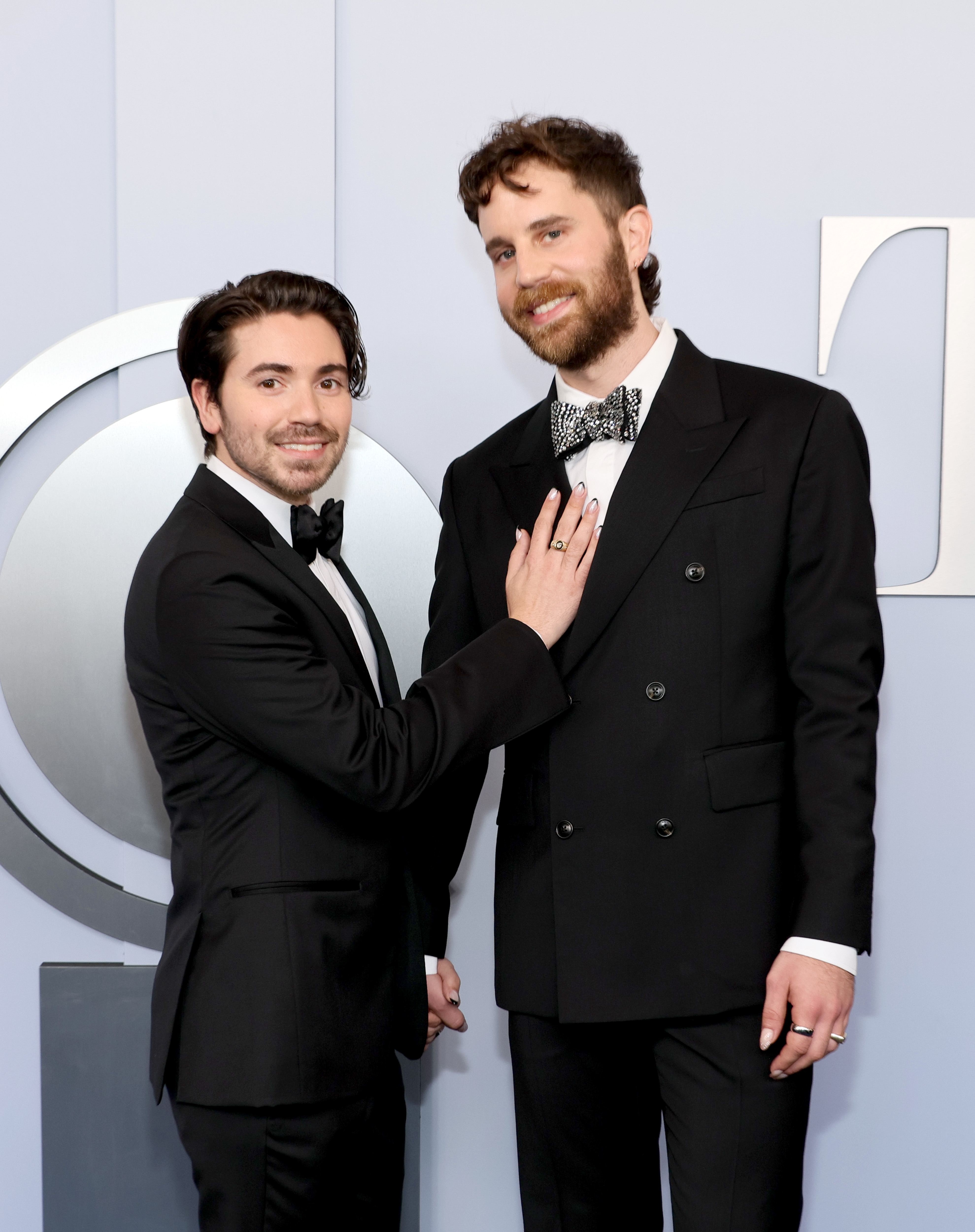 Noah Galvin and Ben Platt pose together on the red carpet, both wearing tuxedos. Noah touches Ben's chest while they smile for the camera