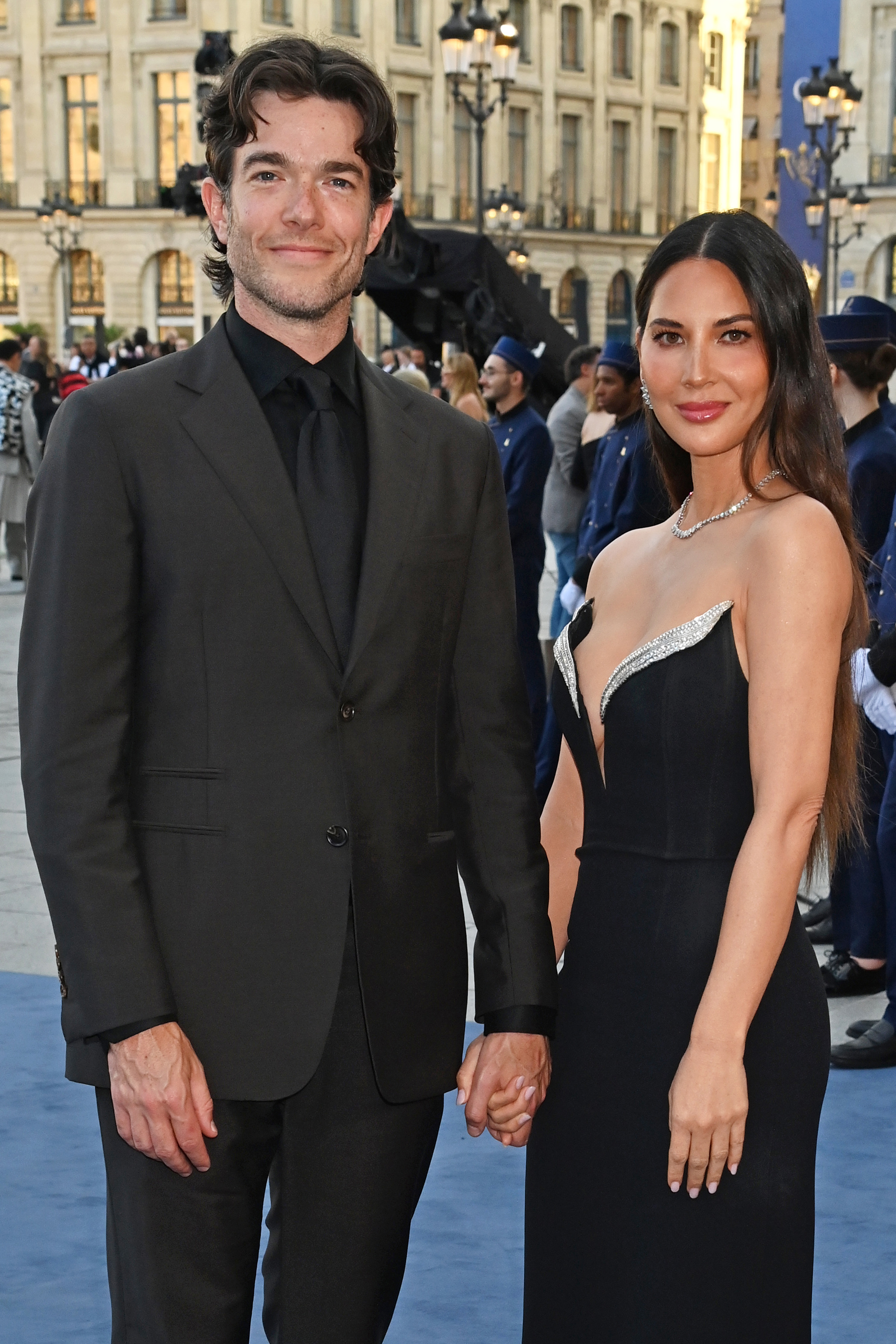 John Mulaney and Olivia Munn at a public event, holding hands