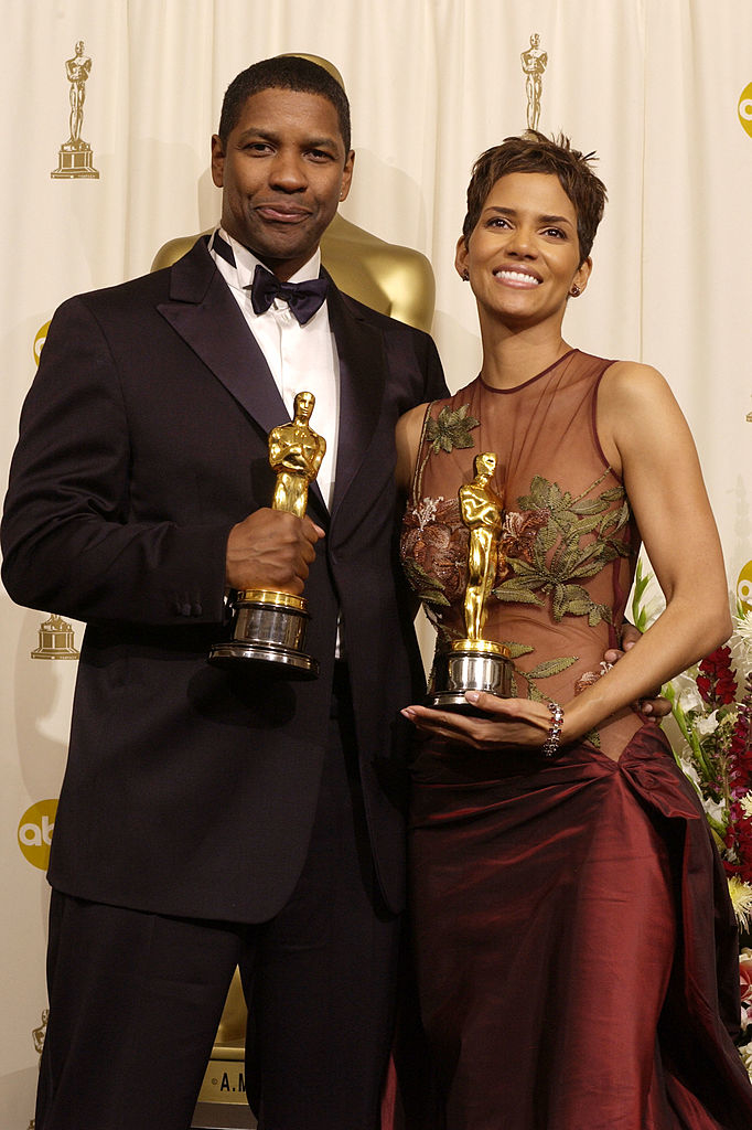 Denzel Washington in a tuxedo and Halle Berry in an elegant gown, both holding their Oscars at the awards ceremony