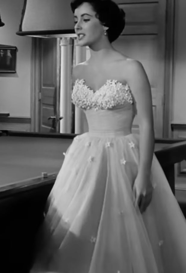 Elizabeth Taylor in a formal gown with intricate detailing, standing next to a pool table