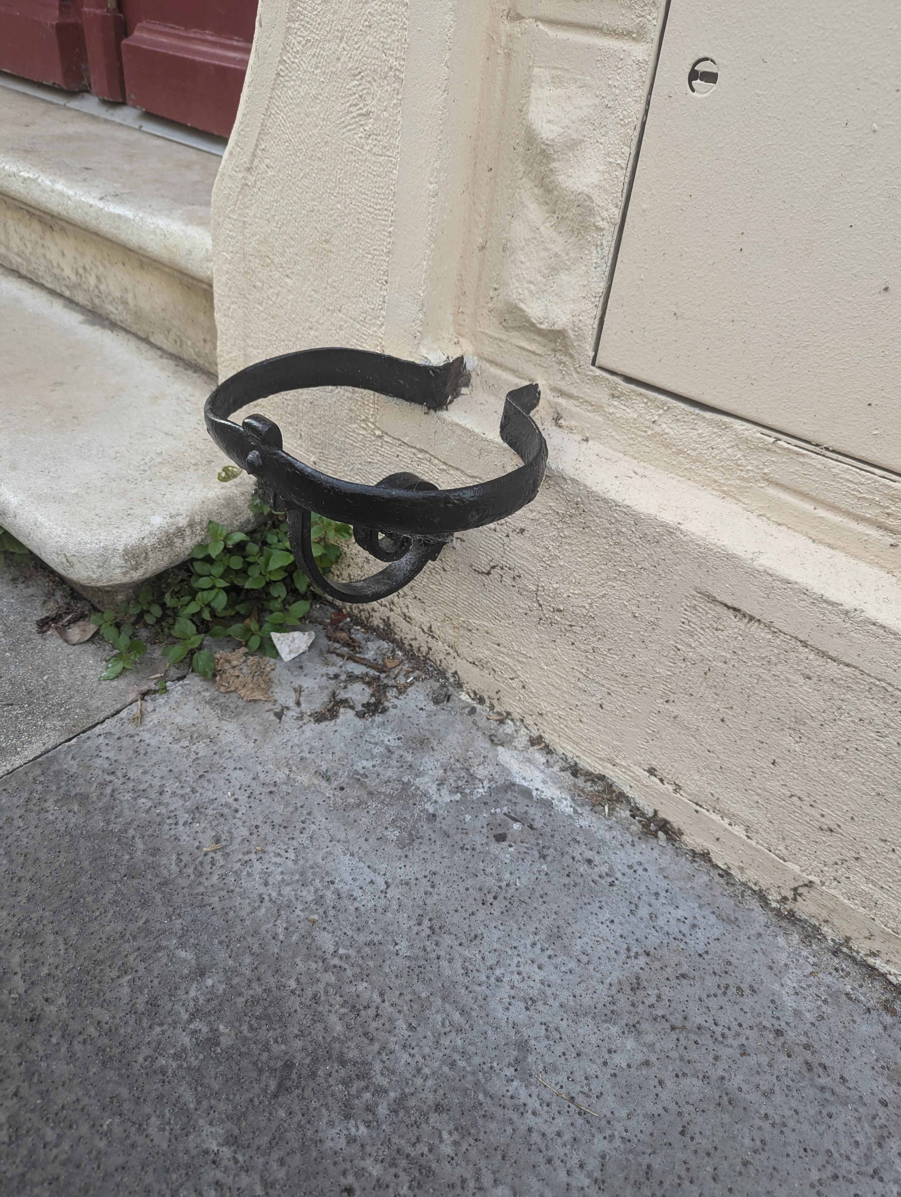 An old metal boot scraper attached to the side of a building near a set of stairs
