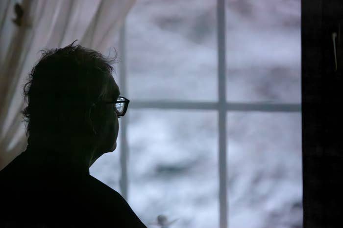 Silhouetted person in glasses looking out a window veiled by gauzy curtains