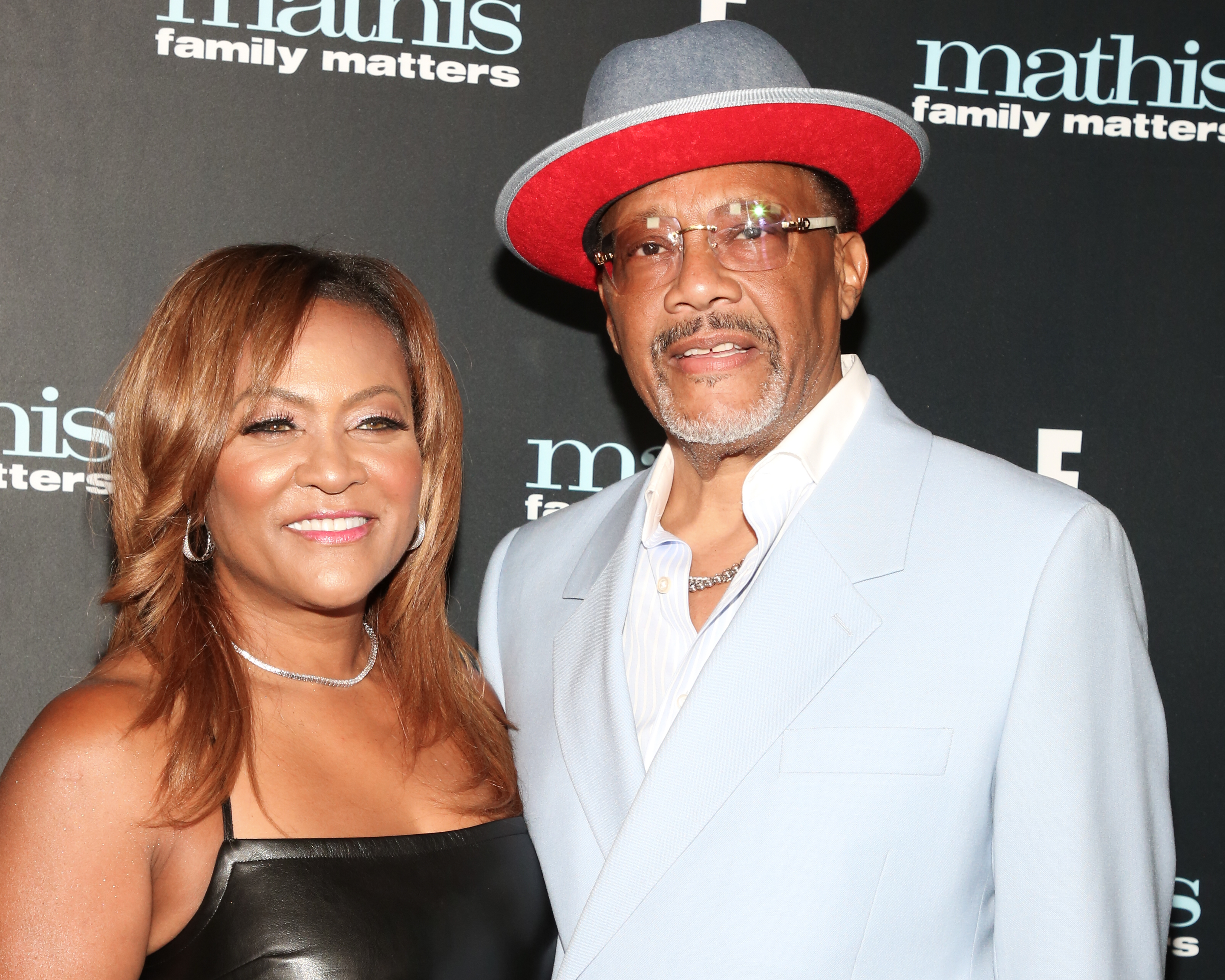 Gregory and Linda Mathis smiling at a 'Mathis Family Matters' event, Gregory in a light suit and hat, Linda in a sleeveless dress