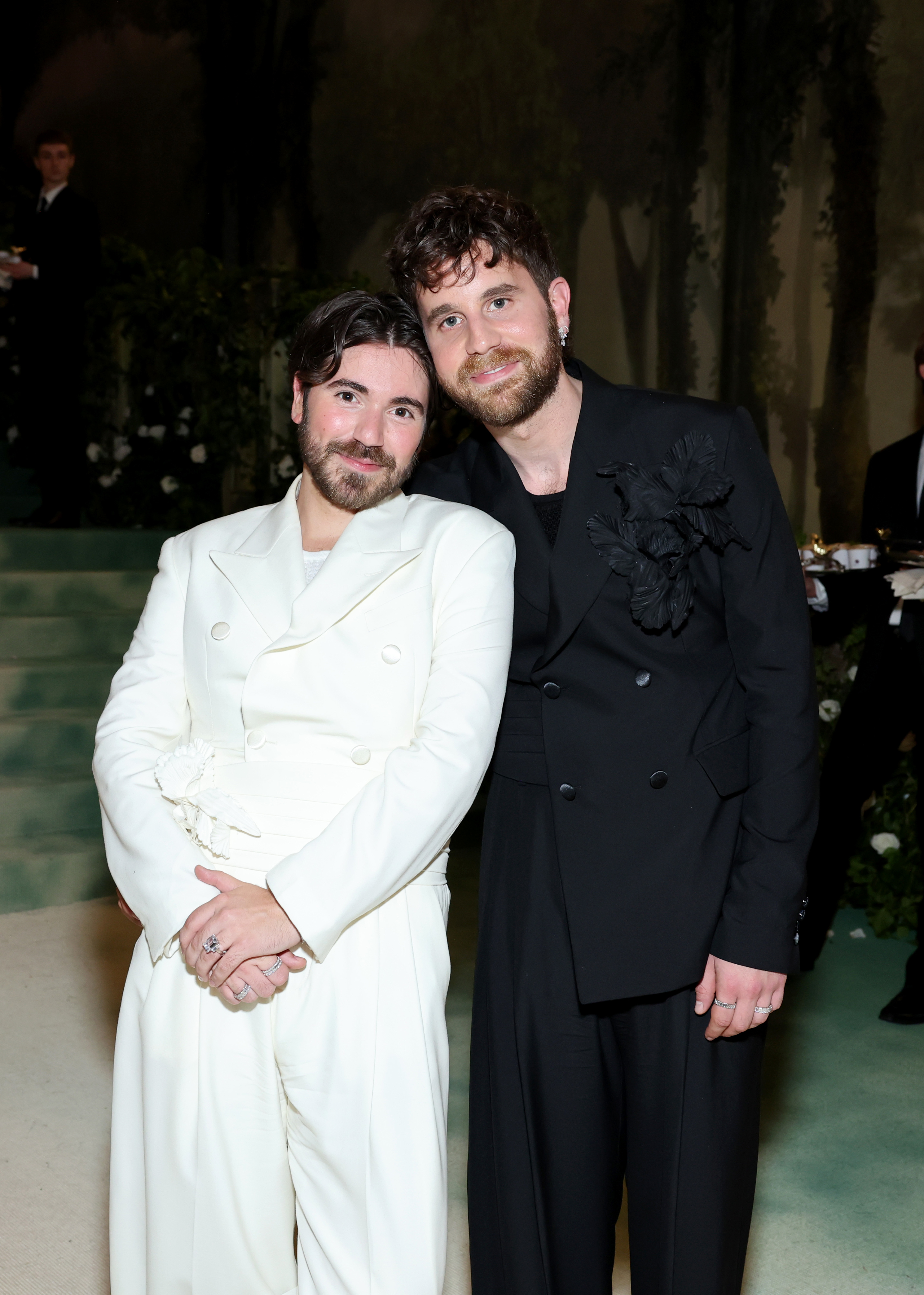Ben Platt and Noah Galvin posing together, Ben in a double-breasted suit and Noah in a suit with a tied waist, at a formal event