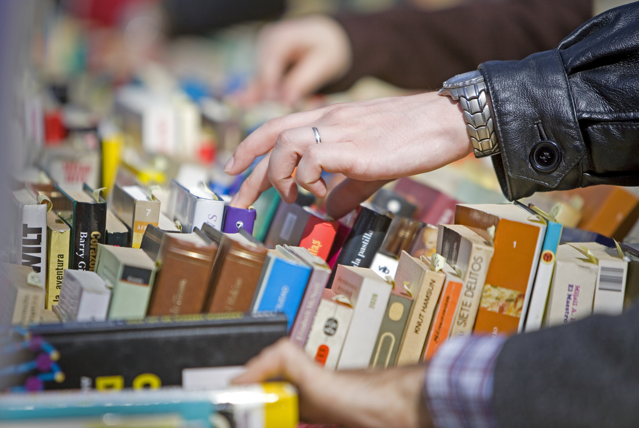 Close-up of hands browsing through a variety of books on a table