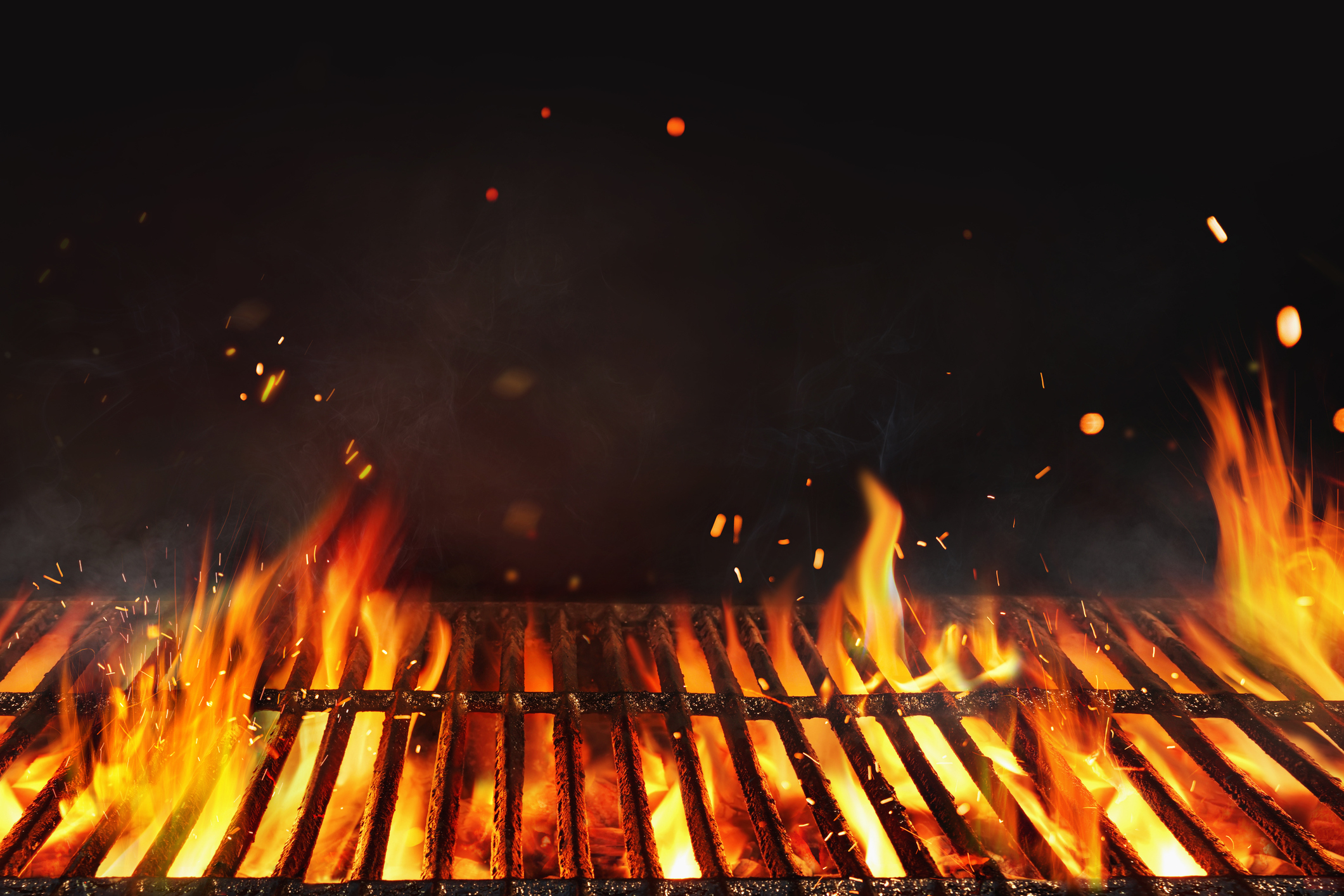 Close-up of a flaming grill with visible sparks and glowing embers, suggesting cooking or a barbecue in progress