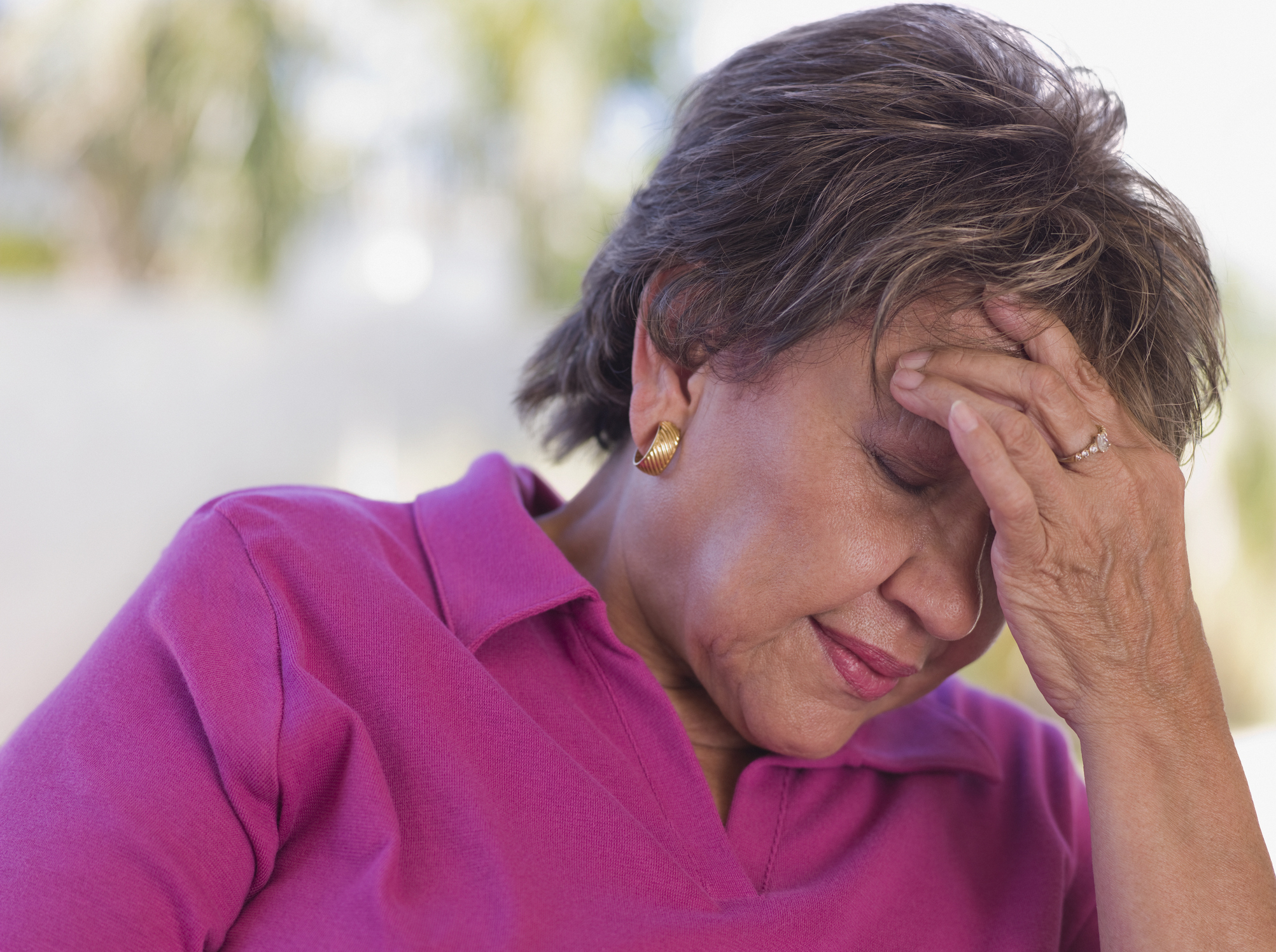 A woman wearing a collared shirt holds her head in her hand with a pained expression on her face