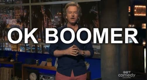 David Spade stands on a TV show set. Text overlay reads "OK BOOMER"