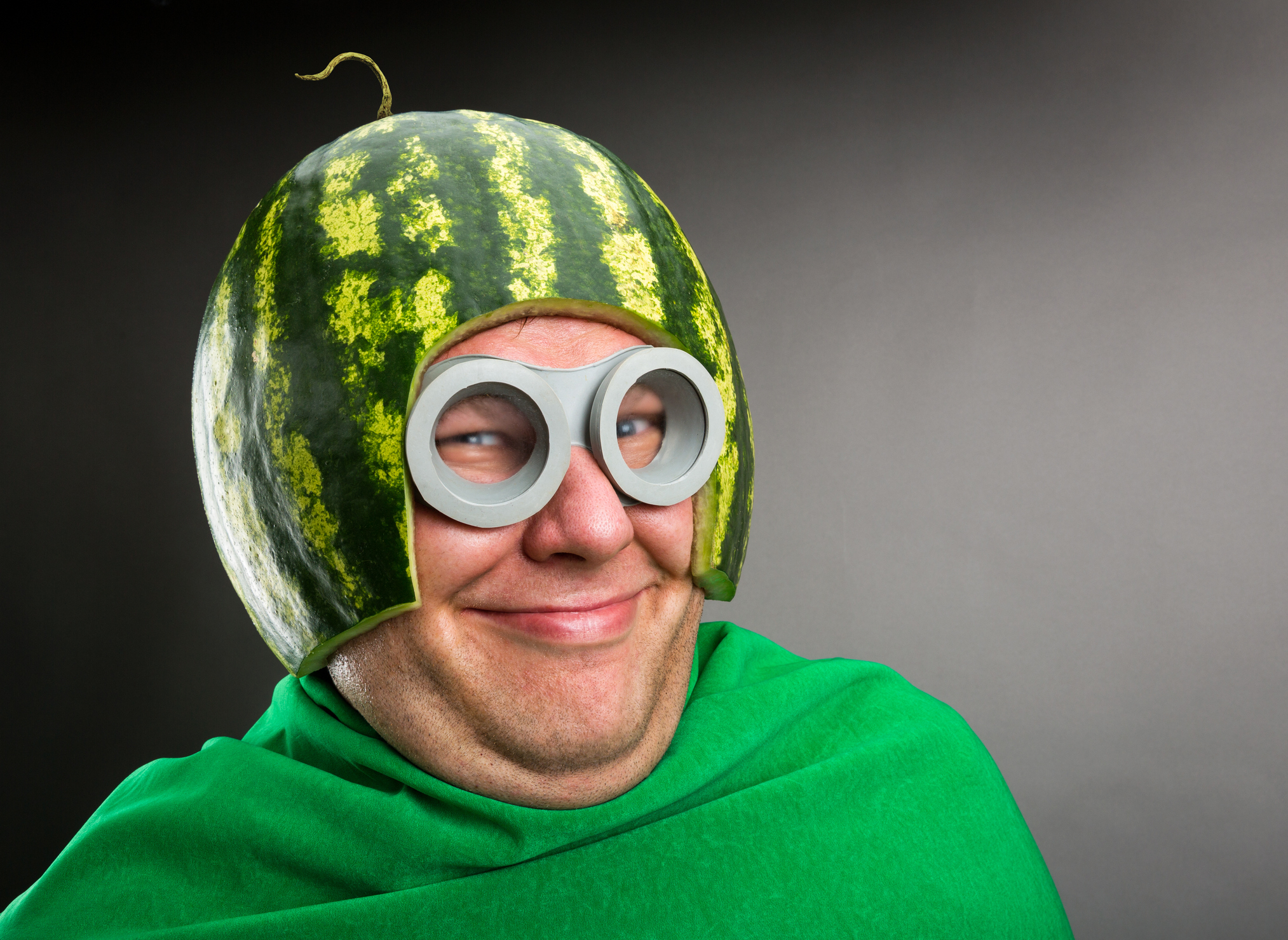 Man wears a watermelon helmet, goggles, and a green cloak, smiling playfully. This humorous image is used in an article categorized as Internet Finds. No names provided
