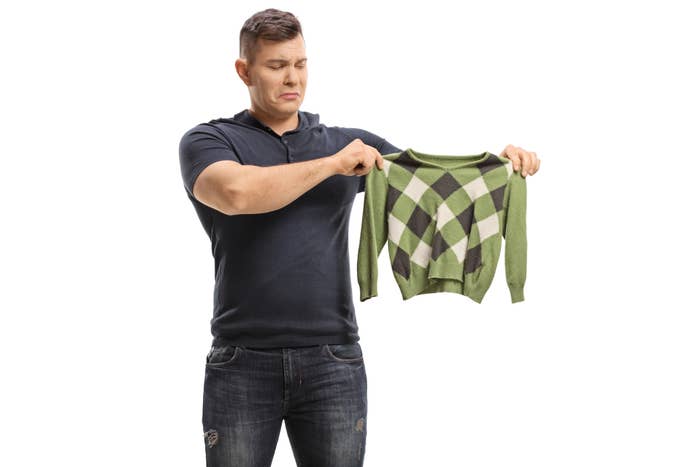 A man holds up a small, argyle-patterned sweater with a displeased expression