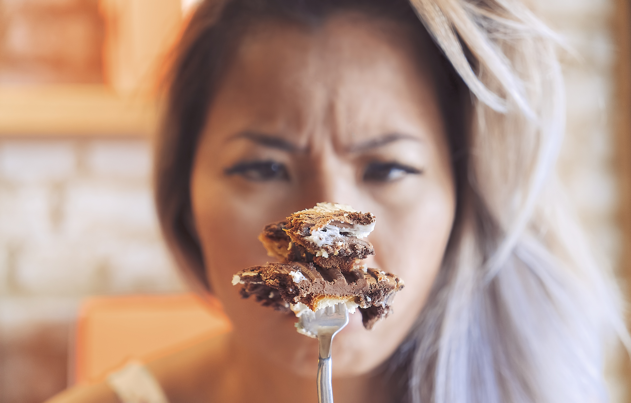 A woman looks intensely at a fork with a piece of chocolate dessert on it