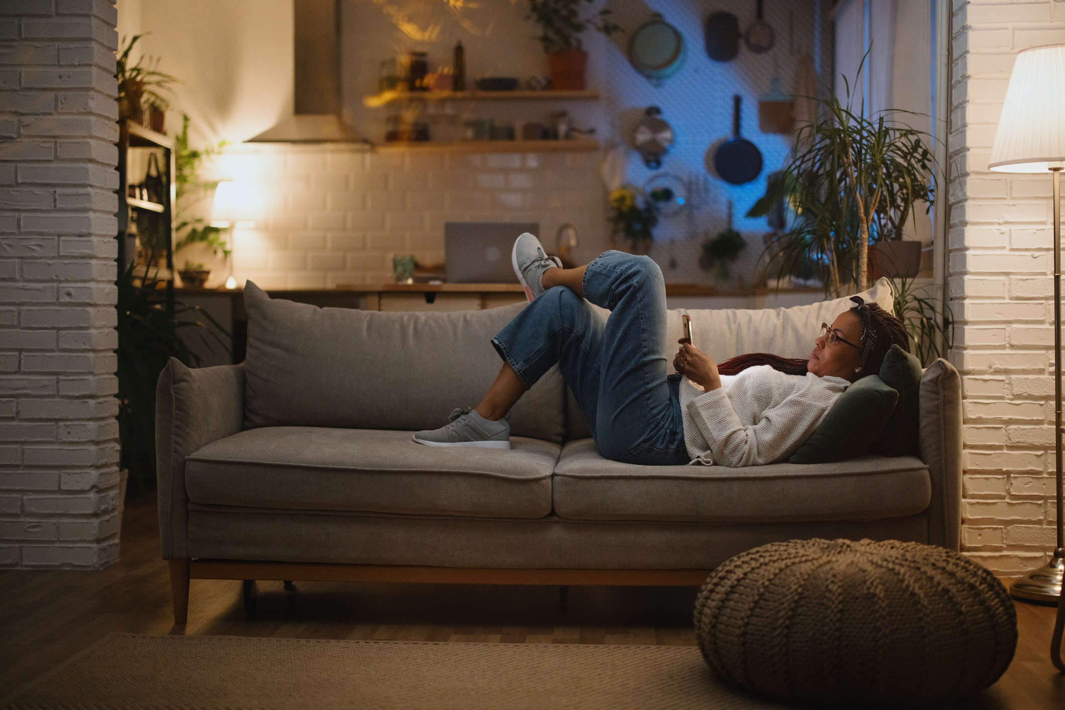 Person relaxing on a couch while reading their phone in a cozy and modern living room with plants and ambient lighting