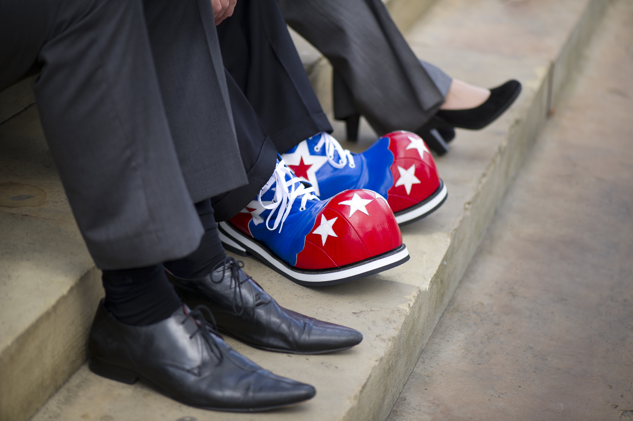 Three adults sitting on steps, one of whom is wearing large clown shoes with star patterns