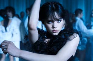 Jenna Ortega intensely dances in a crowded room, showcasing her dramatic dark outfit with ruffled details in a scene reminiscent of an elegant dance event