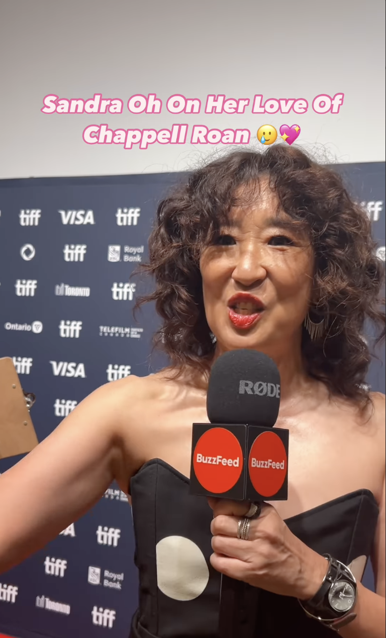 Sandra Oh speaking into a BuzzFeed microphone at a TIFF event, styled in a strapless outfit. The text reads, "Sandra Oh On Her Love Of Chappell Roan."