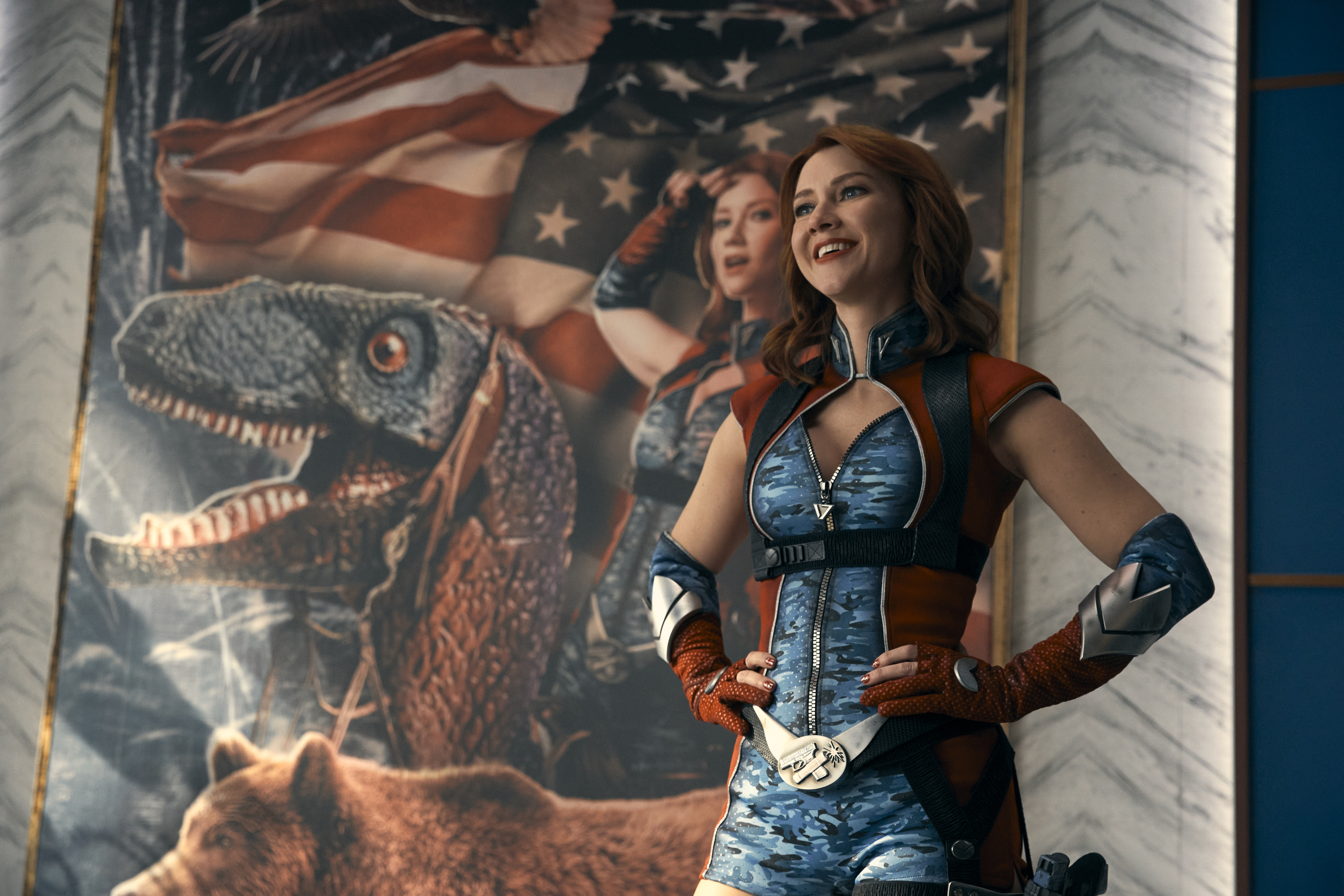 Valorie Curry dressed as her character in "The Boys," in front of a patriotic poster featuring a dinosaur and an American flag