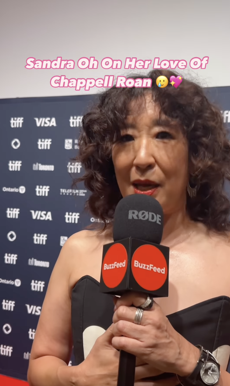 Sandra Oh on a carpet event, holding a BuzzFeed microphone with a "TIFF" backdrop. Text says, "Sandra Oh On Her Love Of Chappell Roan ??"