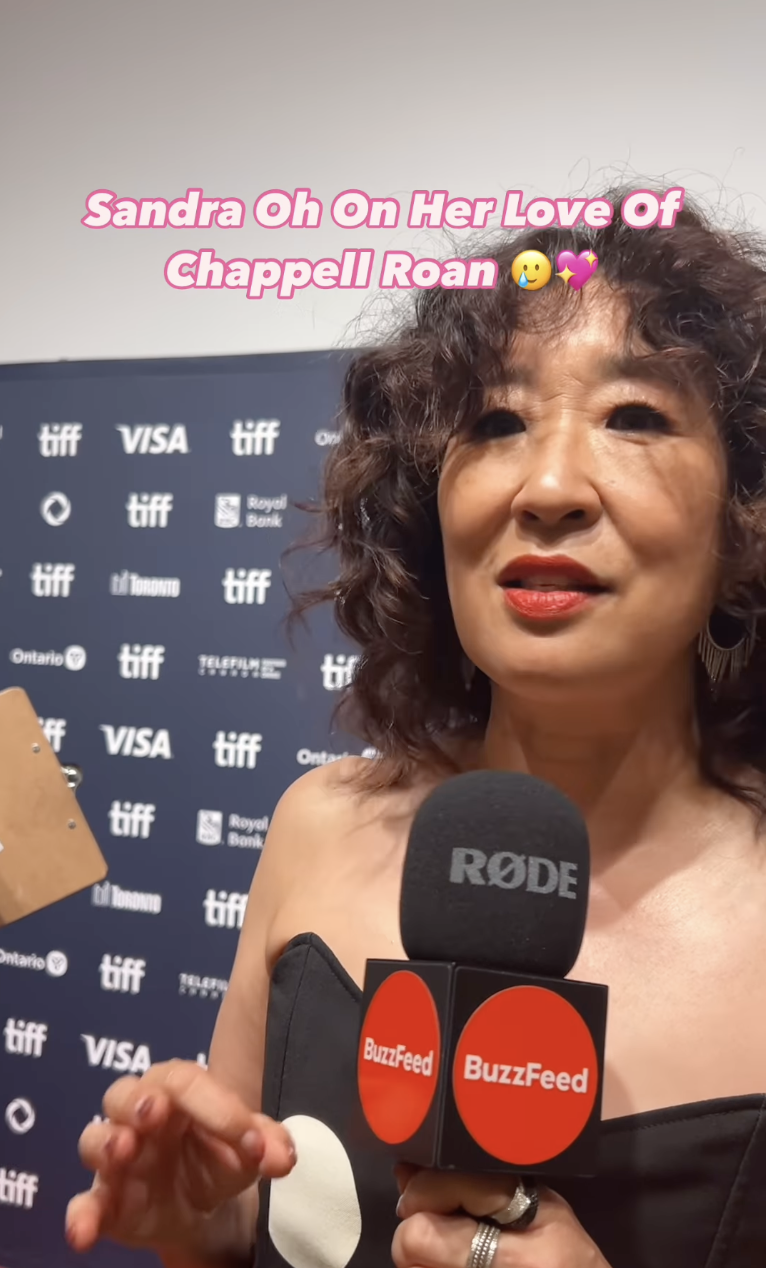 Sandra Oh speaks into a microphone for a BuzzFeed interview at a TIFF event. Text: "Sandra Oh On Her Love Of Chappell Roan."