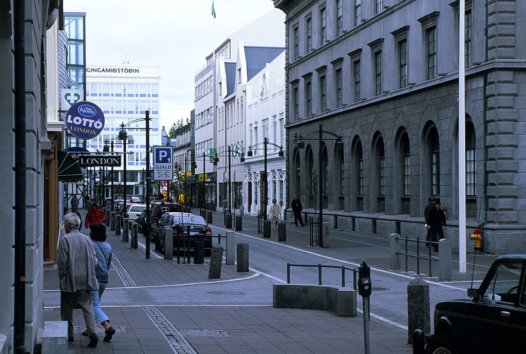City street view with pedestrians, shops, parked cars, and gray buildings in Reykjavik, Iceland