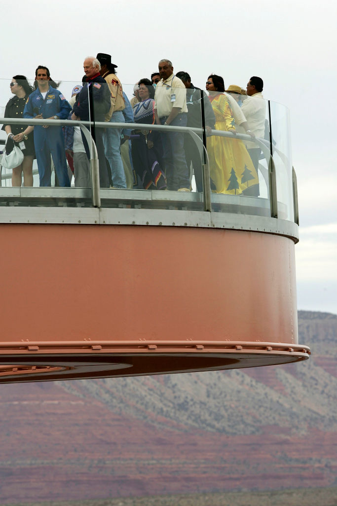 A group of people are standing on a glass bridge at the Grand Canyon Skywalk, enjoying the scenic view