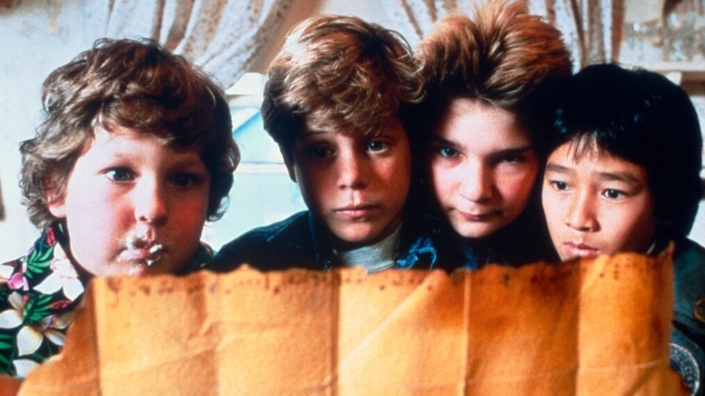 Jeff Cohen, Sean Astin, Corey Feldman, and Ke Huy Quan curiously look at a mysterious, old map
