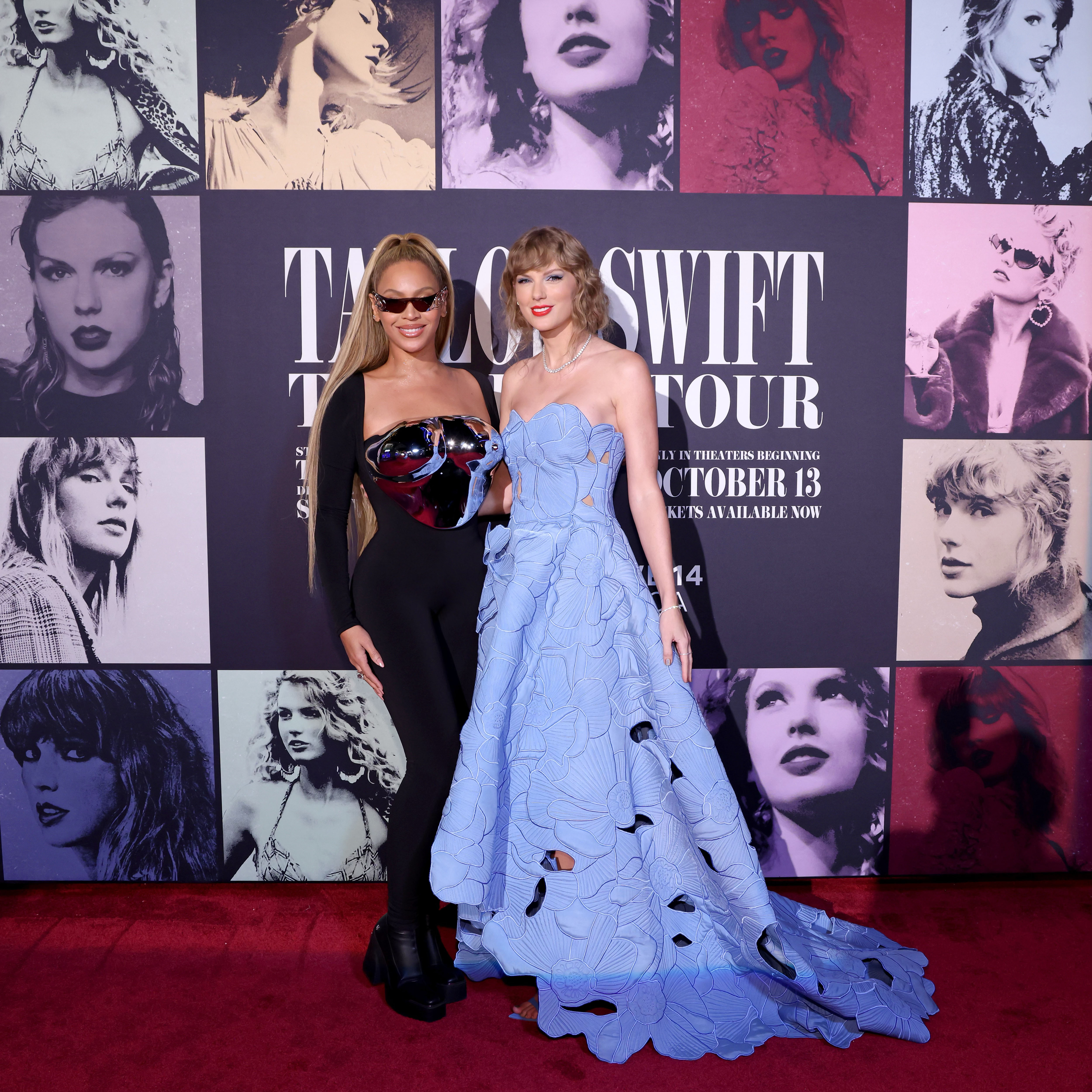 Beyoncé y Taylor Swift en la alfombra roja. Beyoncé lleva traje ajustado negro con detalles de colores. Taylor lleva vestido azul claro con encaje y cortes