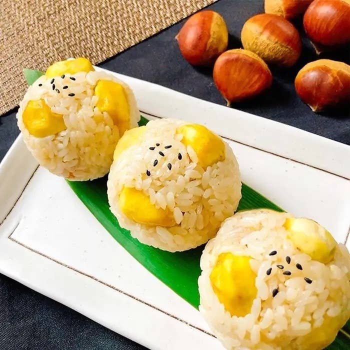 お皿の上に置かれた栗ご飯のおにぎりが3つ並んでいます。背景には栗も見えます。