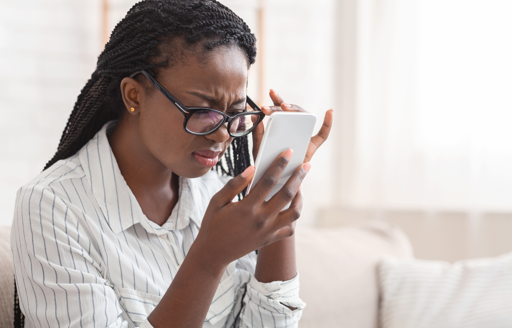 Person with glasses struggling to read small text on a smartphone screen, looking frustrated and holding the phone close to their face