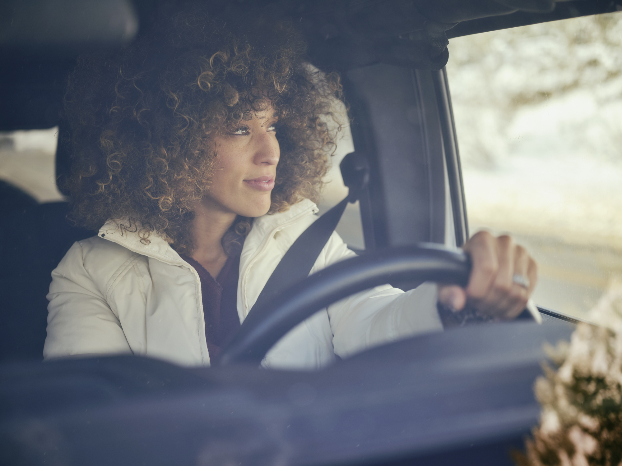 A person with curly hair drives a car, focused on the road ahead
