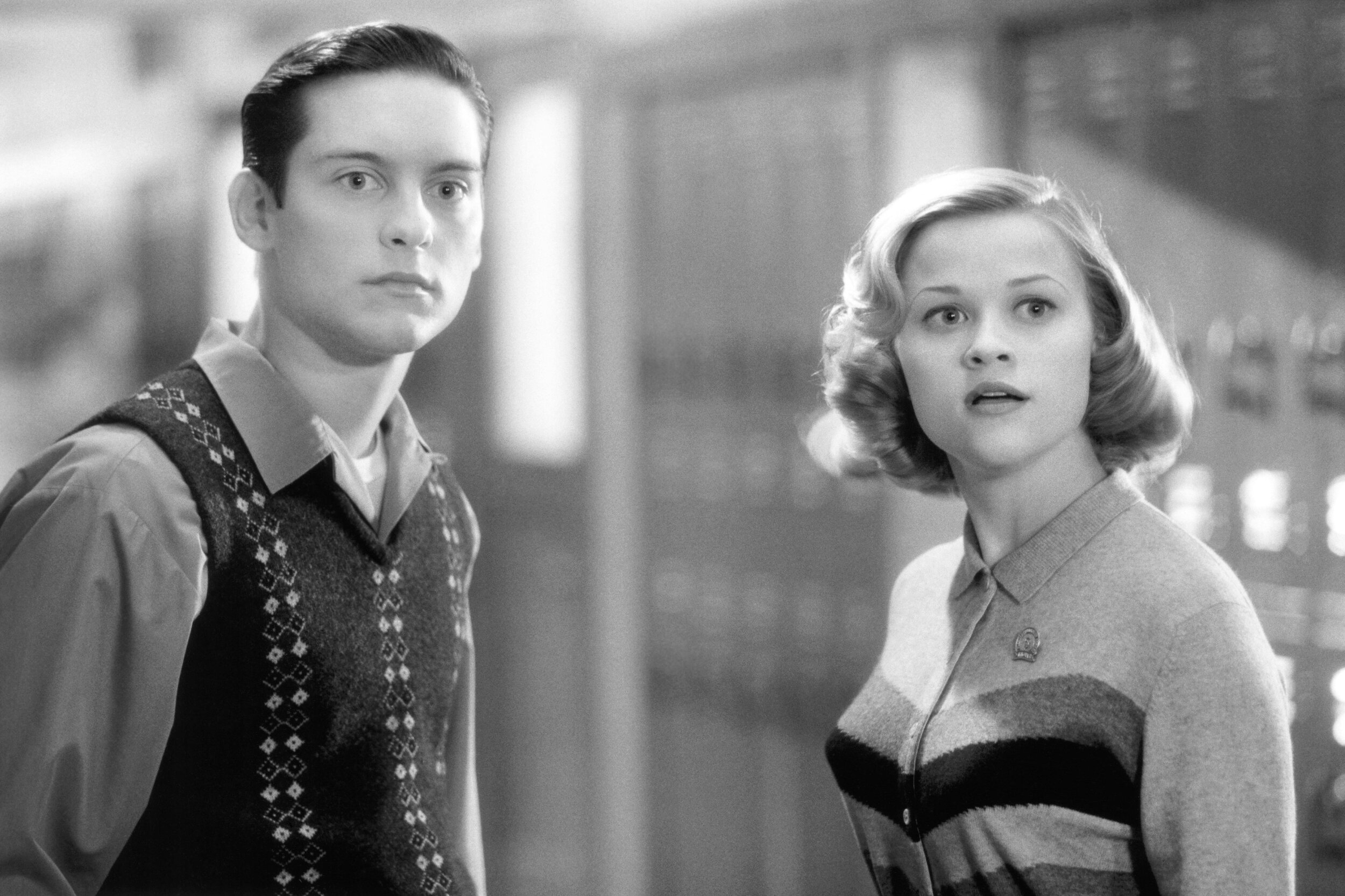 Tobey Maguire and Reese Witherspoon in 1950s-style outfits, standing in front of school lockers, looking surprised