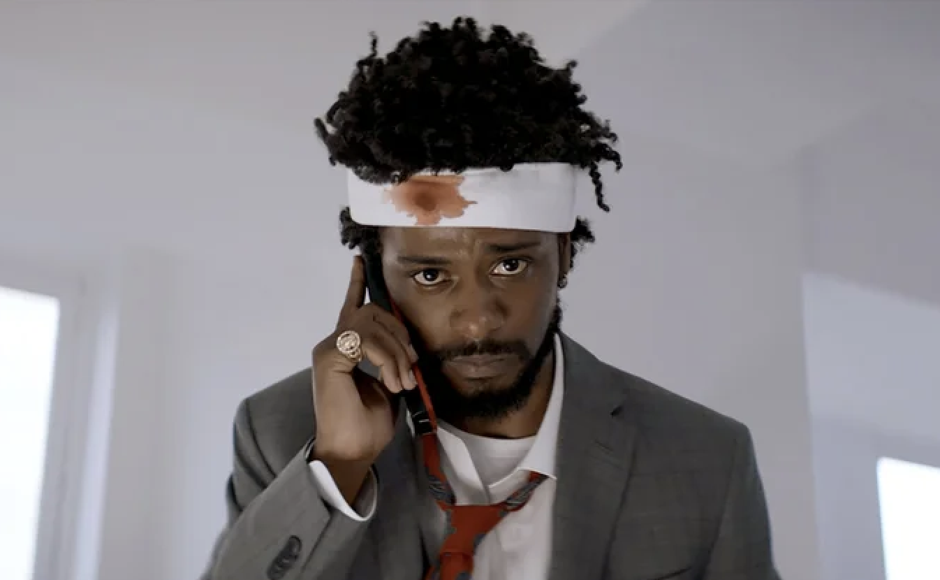 Man with a headband holding a phone to his ear, dressed in a suit with a loose tie and a stained shirt