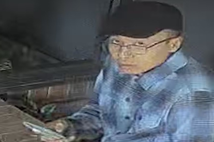 男性が帽子とチェック柄のシャツを着て、携帯電話を手に持ちながら座っている。