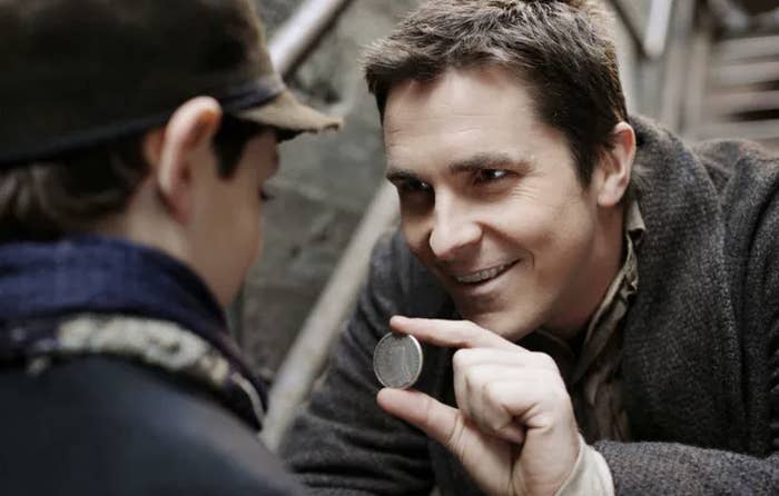 Christian Bale shows a magic coin to a young boy in a scene from a movie