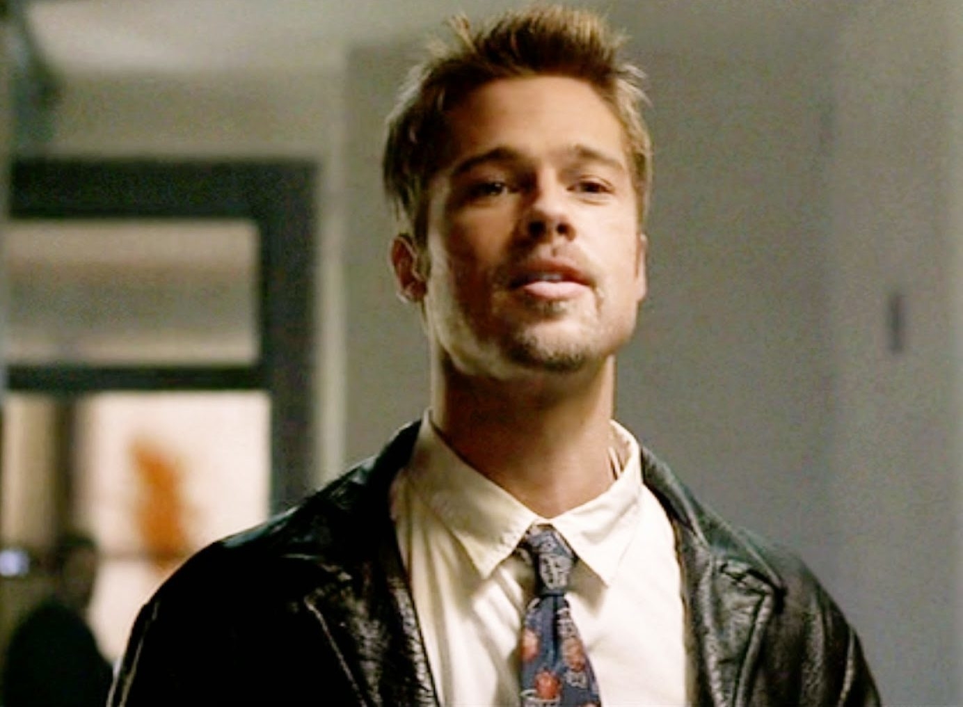 Brad Pitt in a scene from a movie, wearing a leather jacket over a shirt and tie