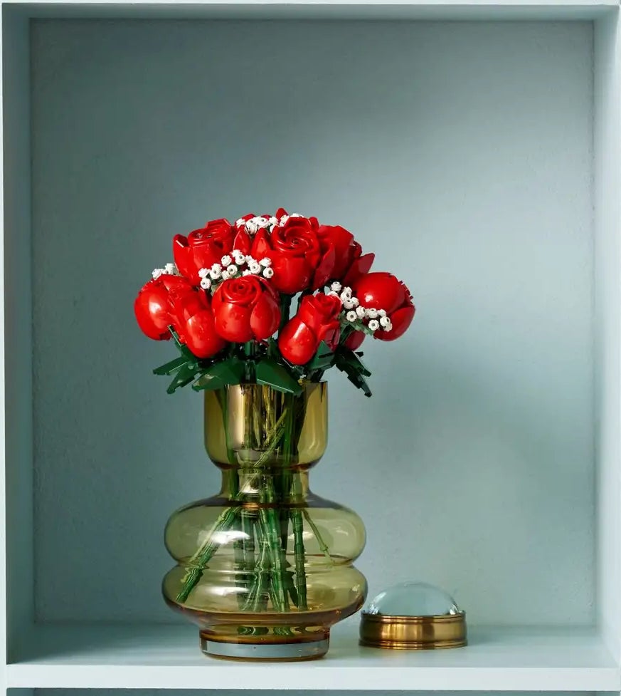 A shelf with various objects, including vases, books, boxes, and a bouquet of red flowers in a green vase