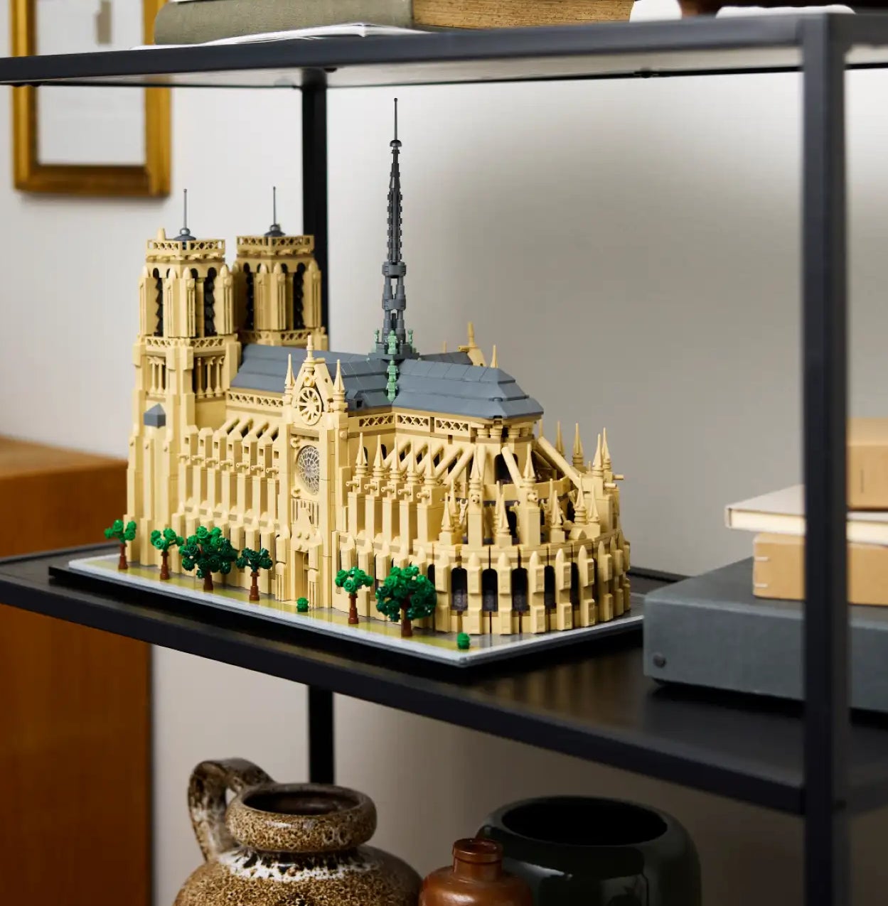 Shelf with a detailed model of Notre Dame Cathedral, surrounded by books, a wooden bowl, decorative pottery, and other small items in a home setting