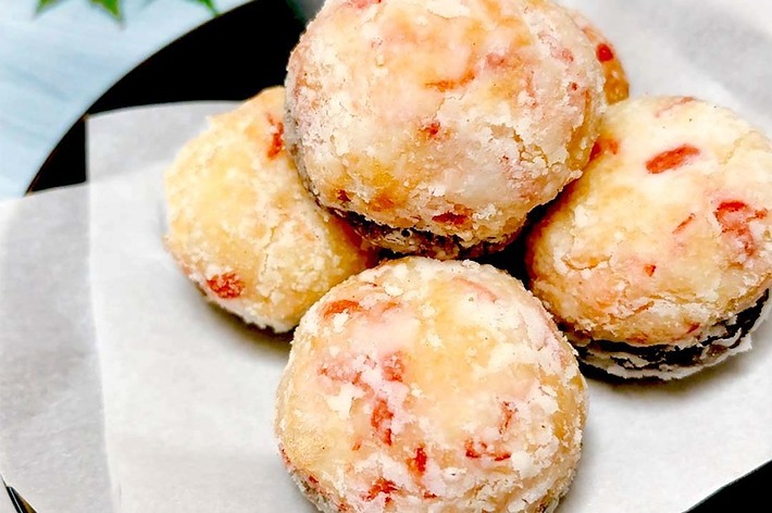 白い皿に載った数個の粉砂糖をまぶした焼き菓子。皿の横には緑の葉が添えられている。