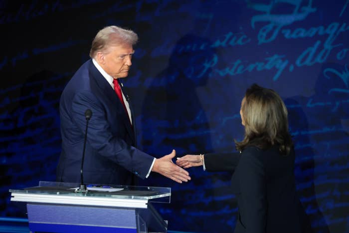 Donald Trump in a suit and tie and Kamala Harris in a blazer shake hands on a debate stage