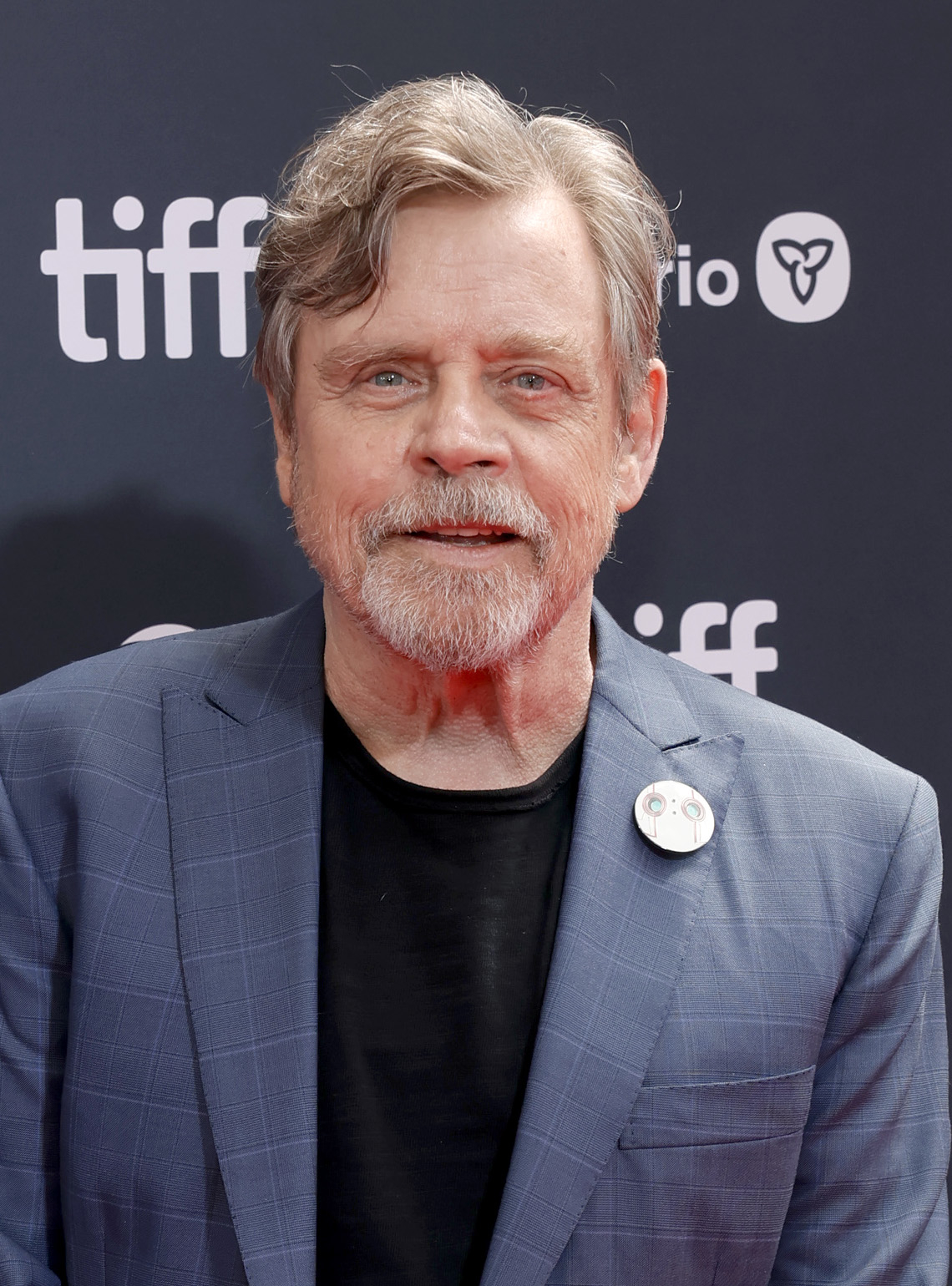 Mark Hamill at the Toronto International Film Festival (TIFF), wearing a blazer and a shirt, standing in front of a branded background