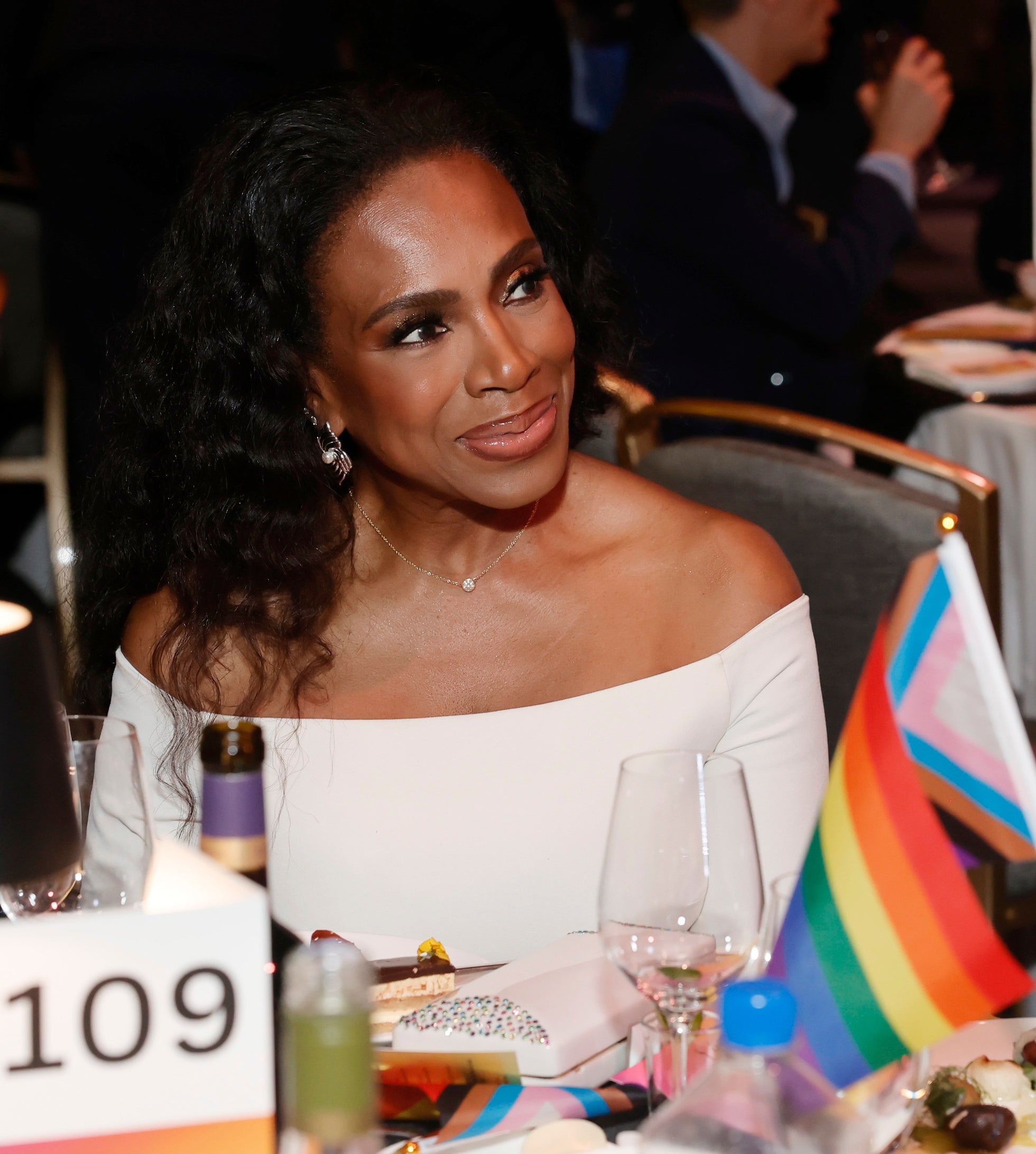 Sheryl Lee Ralph, wearing an off-the-shoulder dress, sits at a table during an event, with a rainbow flag and table number 109 visible