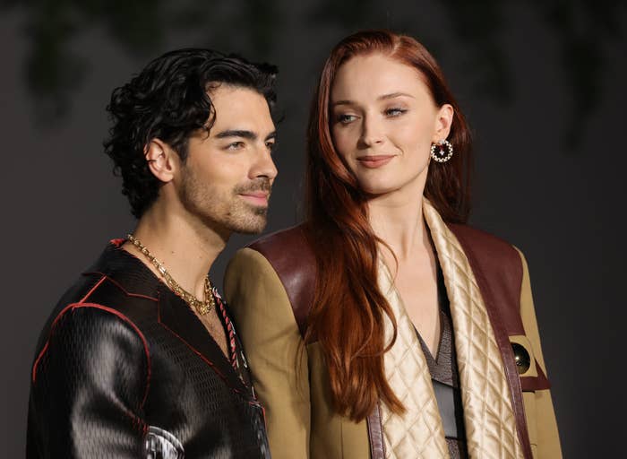 Joe Jonas and Sophie Turner attending an event, Joe in a patterned suit and Sophie in a chic coat with gold accents
