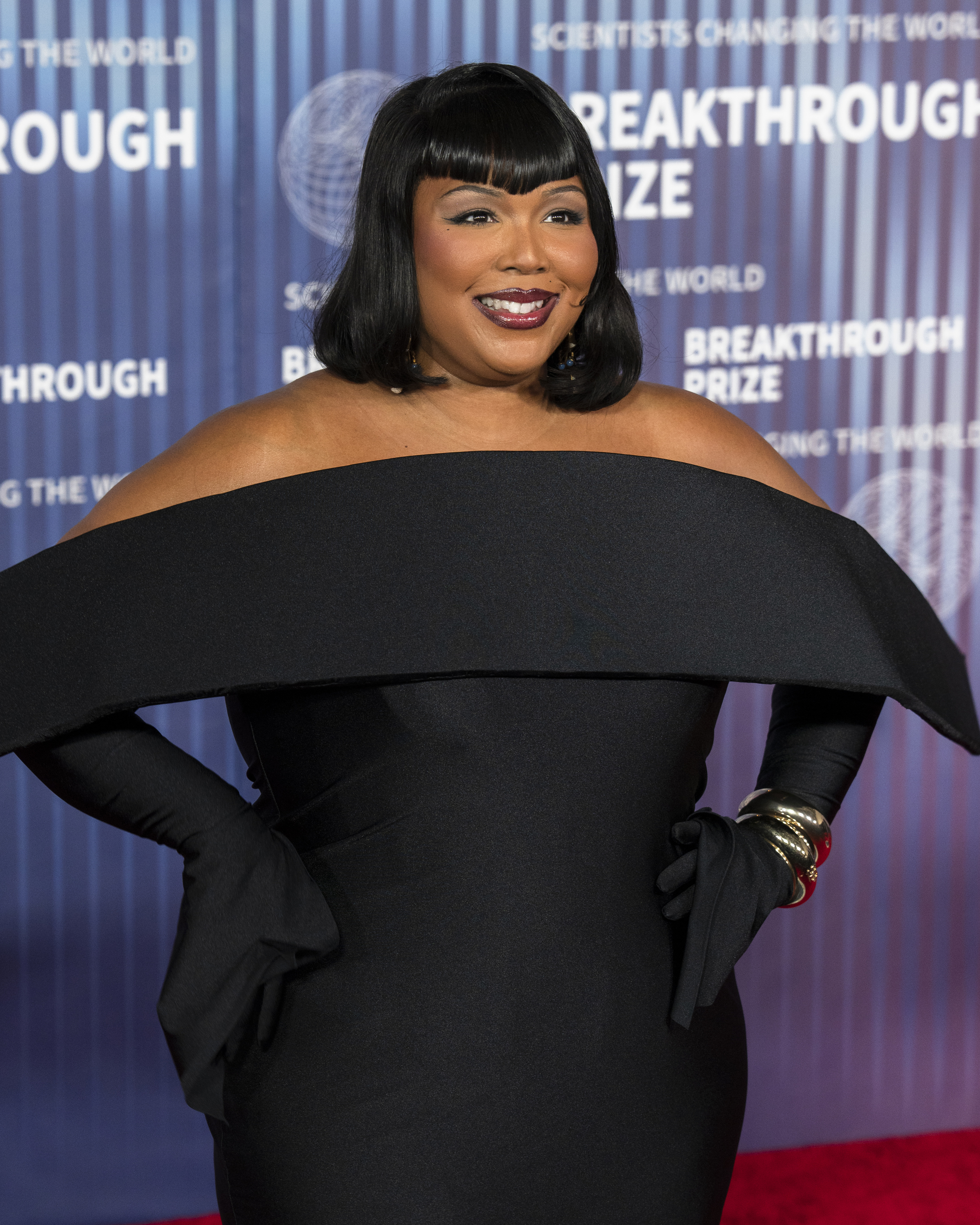 Lizzo poses on the red carpet in an elegant off-shoulder dark dress with long gloves at the Breakthrough Prize event