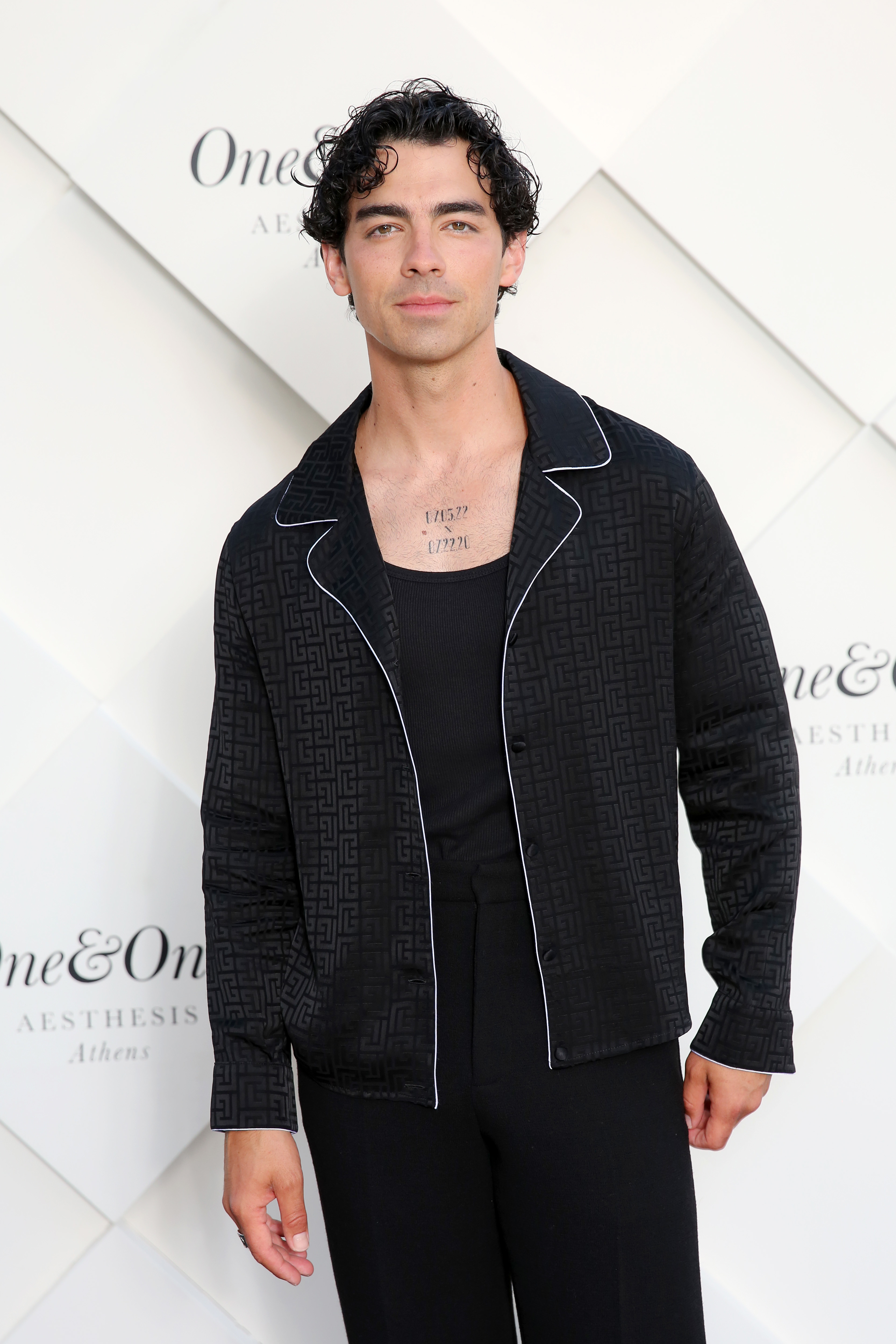 Joe Jonas at an event wearing a dark patterned suit with a black undershirt