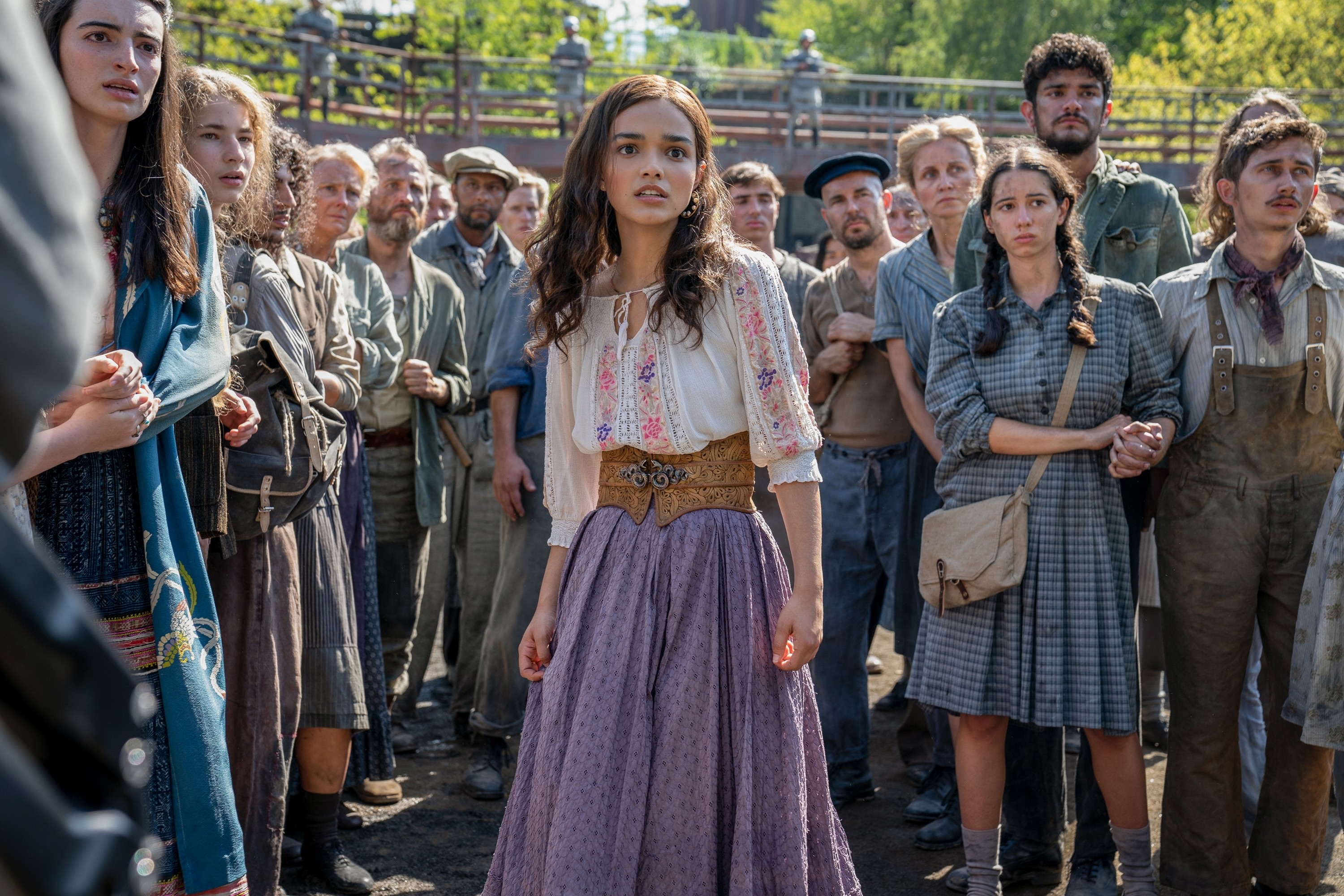 Scene from "The Hunger Games: The Ballad of Songbirds and Snakes" with Rachel Zegler as Lucy Gray Baird, surrounded by a crowd dressed in rustic attire