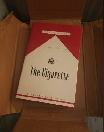 A book titled "The Cigarette: A Political History" by Sarah Milov lies in an open cardboard box