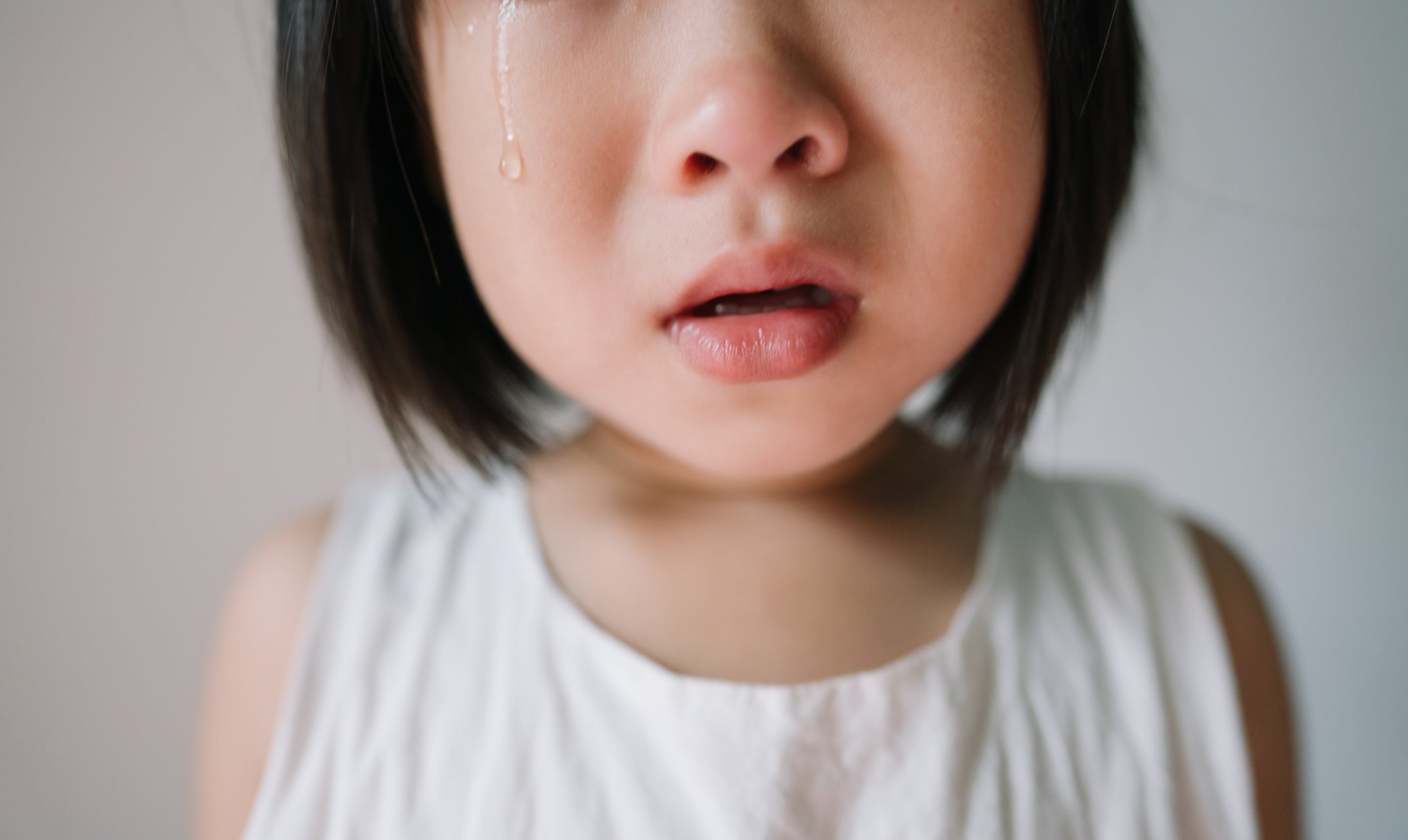 A young child with tears streaming down their face looks distressed while wearing a sleeveless shirt